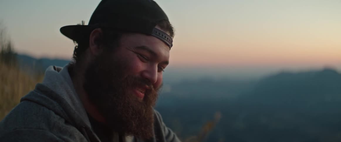 A man is sitting outside laughing in a mountain setting after the sun has set