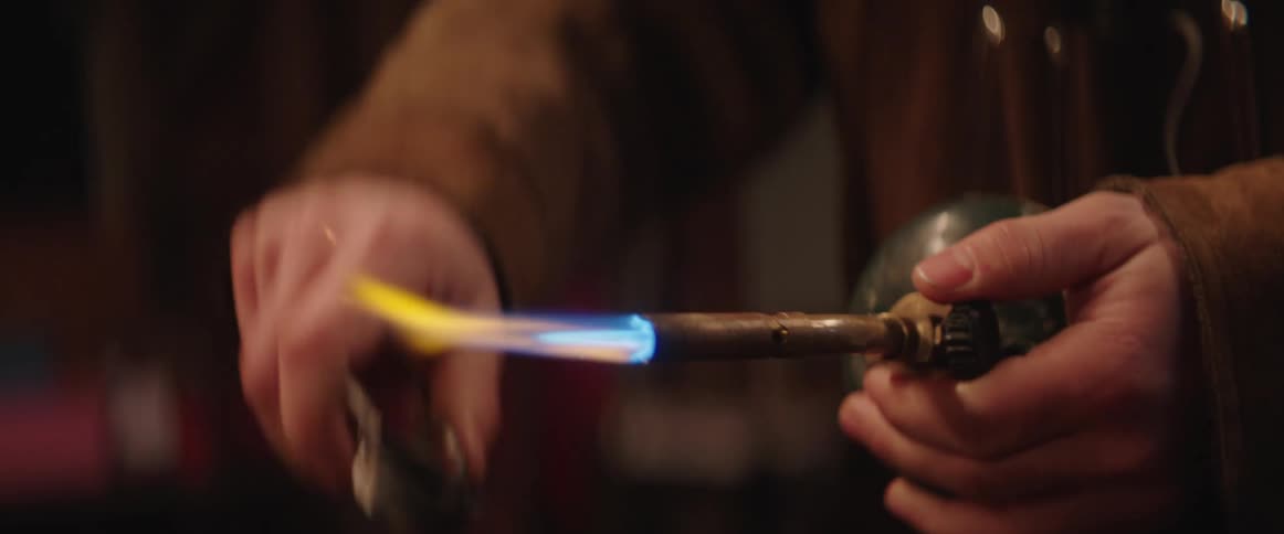 Close up of the hands of a man lighting a propane torch with a flint spark igniter