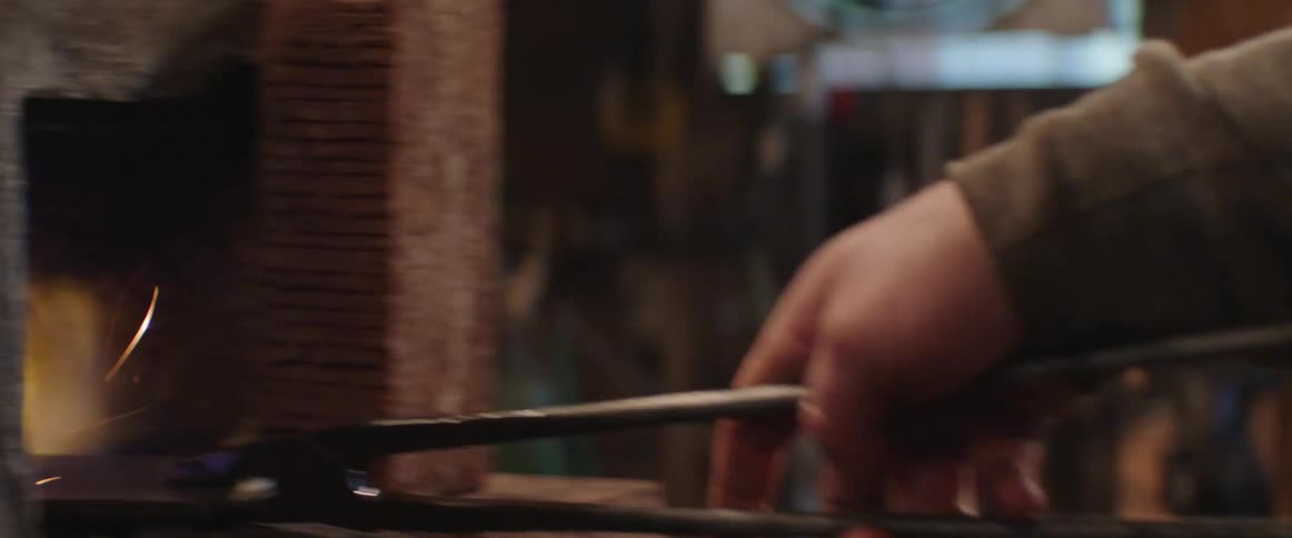 Blacksmith uses a pair of tongs to bring a piece of raw iron from an anvil to the forge
