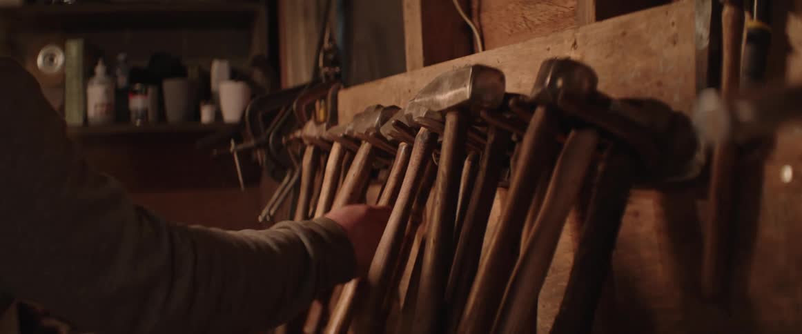 A person is grabbing a hammer from a workshop wall