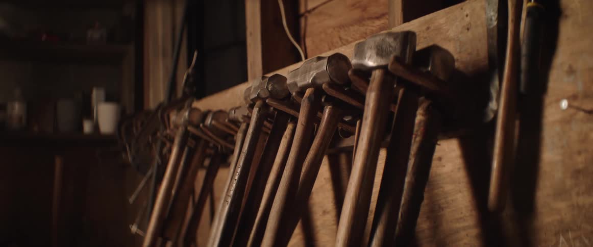 Many hammers are hanging on a rack on the wall of a blacksmith workshop