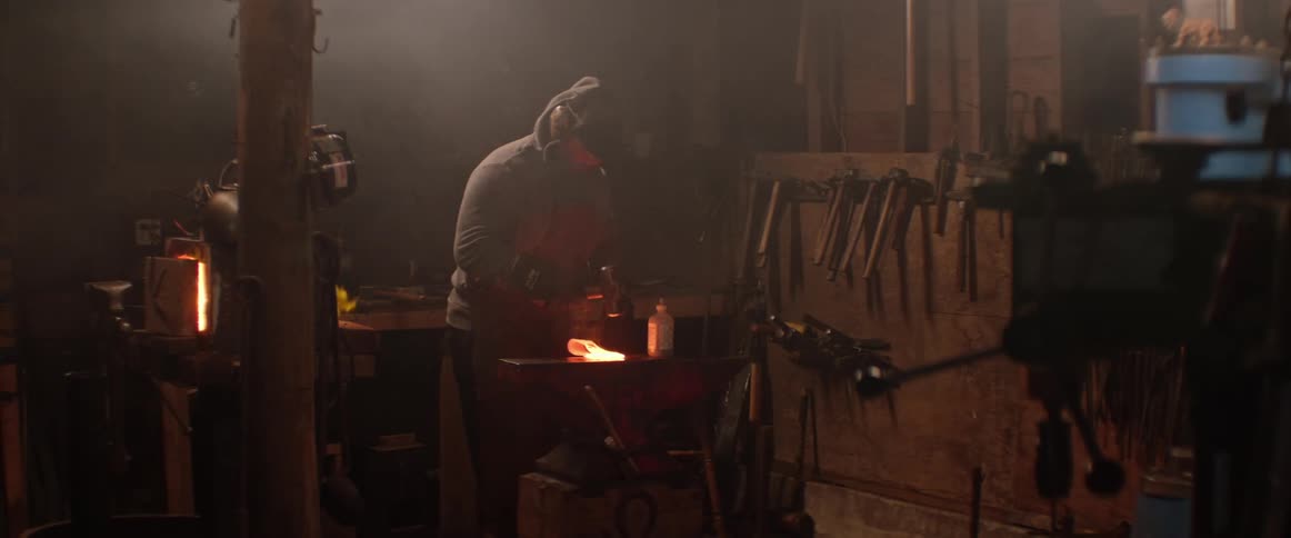 Blacksmith hits a red hot axe head with a hammer creating exploding sparks