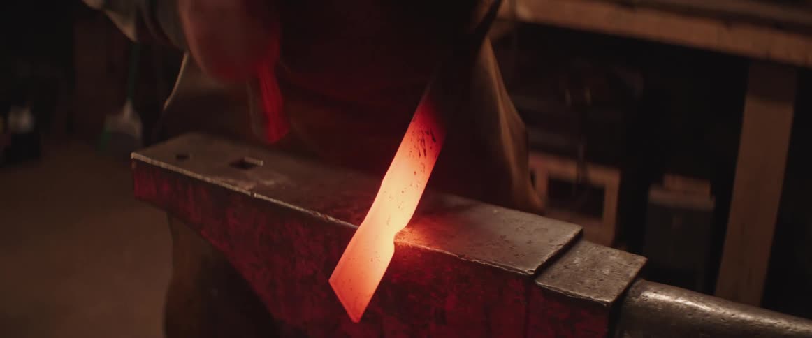 The blacksmith hammers a piece hot metal on an anvil