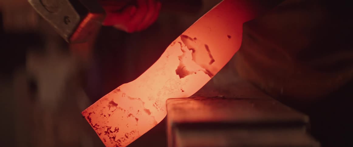 Blacksmith shapes metal by heating it in a fire and hitting it with a hammer