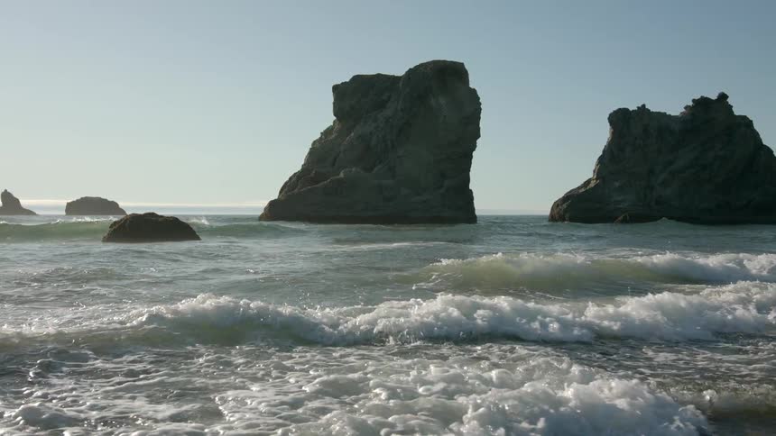 Waves splash against rocks in the water as they roll into shore under a clear sky
