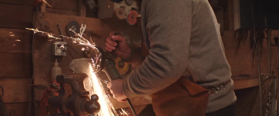 Man cuts a piece of metal over a workbench using a grinder tool