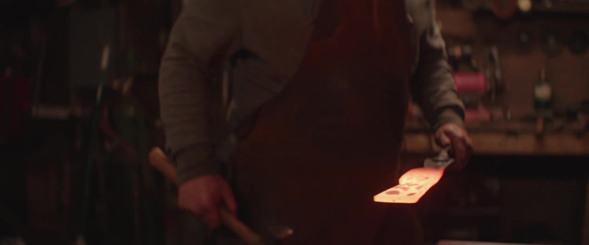Blacksmith uses a pair of tongs to bring a piece of red hot iron from the forge to an anvil
