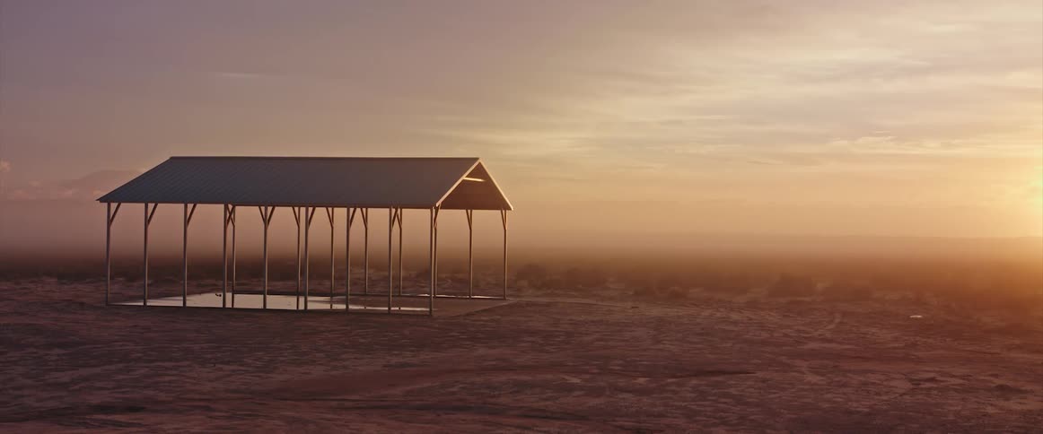 An open pavilion building stands with the sun on the horizon in a hazy sky