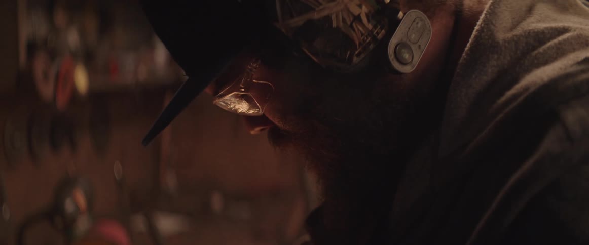A blacksmith's face lights up as sparks shoot across his workbench
