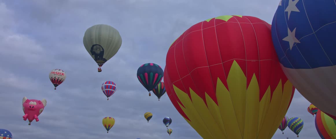 Several colorful hot air balloons float in an overcast sky