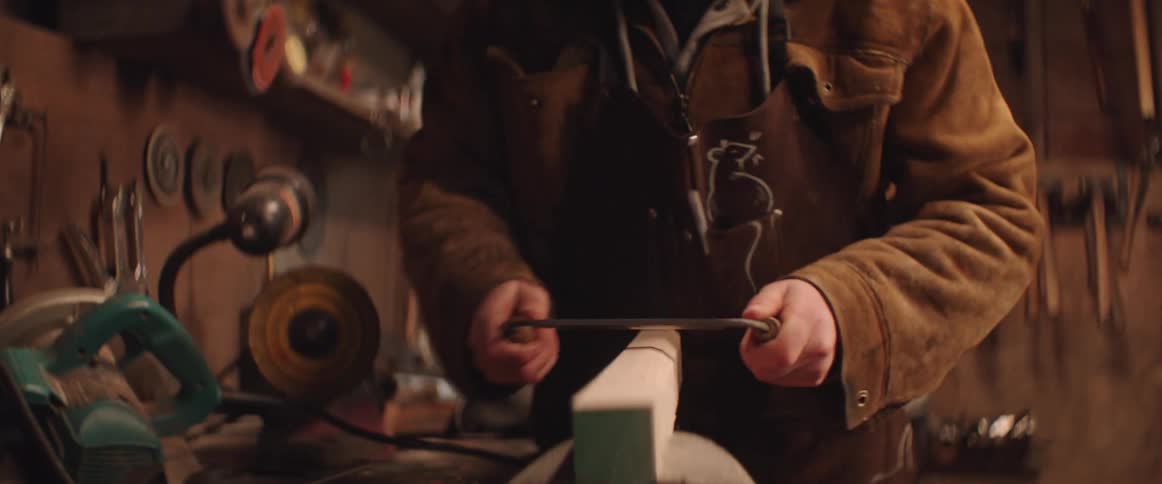 Blacksmith trims the edges of a plank of wood in the workbench in his workshop
