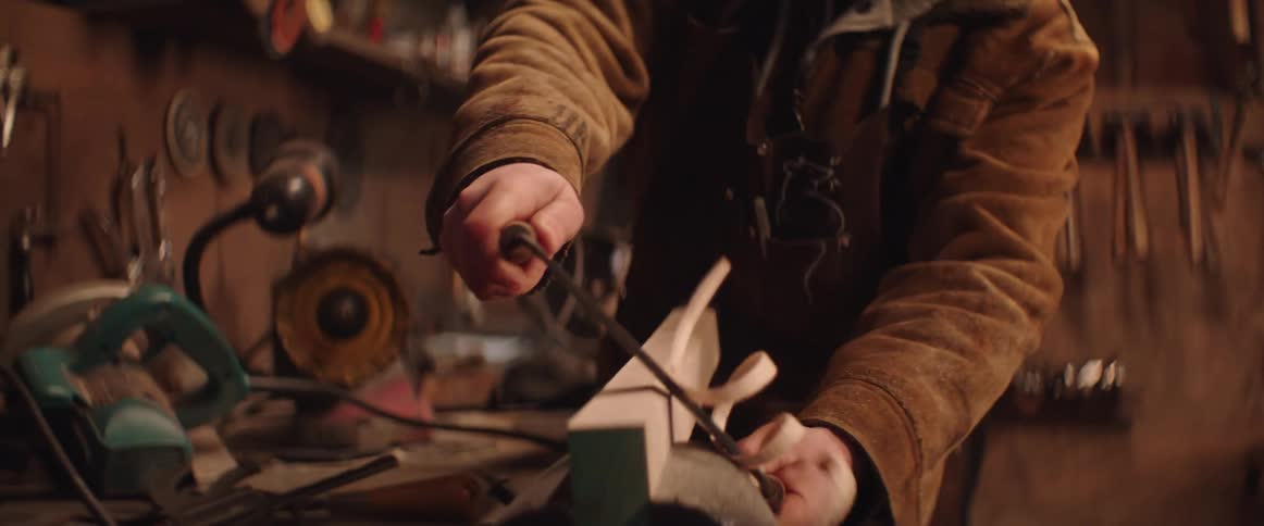 Carpenter trims the edges of a plank of wood in the workbench at his workshop
