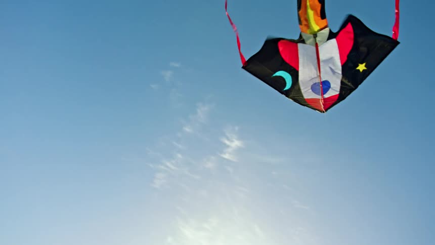 The sun is shining on a colorful kite flying in a blue sky