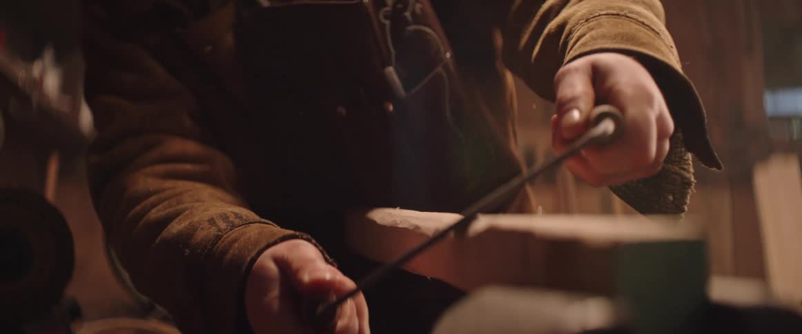A man shaves the edges of a long piece of wood to make an axe handle