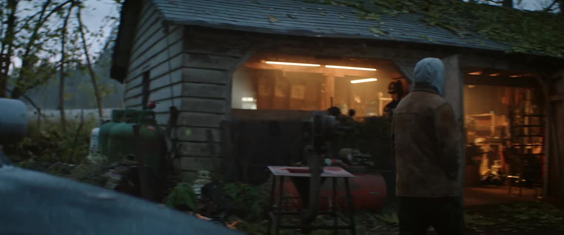A man wearing a hoodie gets out of a truck and walks towards his workshop in the morning