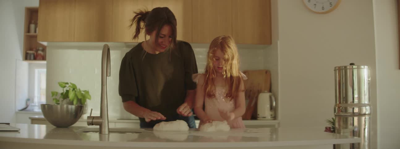 A woman and child are kneading dough in the kitchen