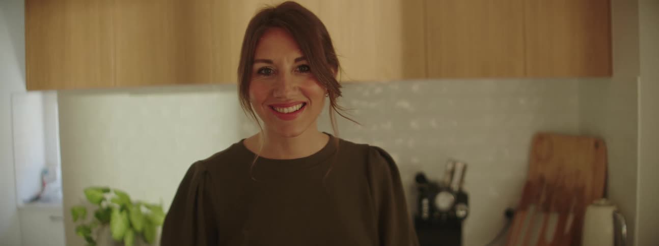 Woman with brown ponytail and dark green blouse smiles at camera in the kitchen