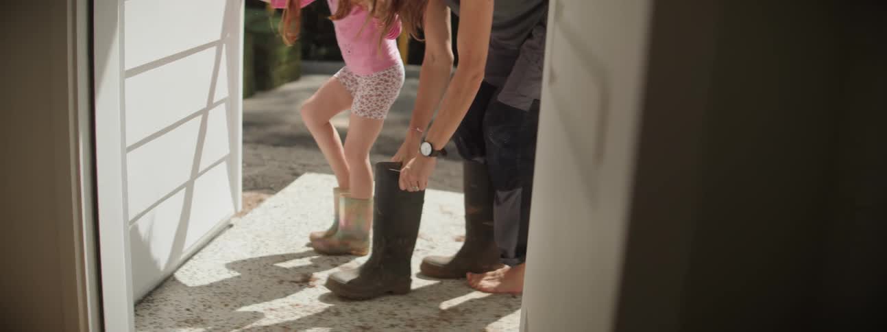 A mother and daughter outside putting on boots
