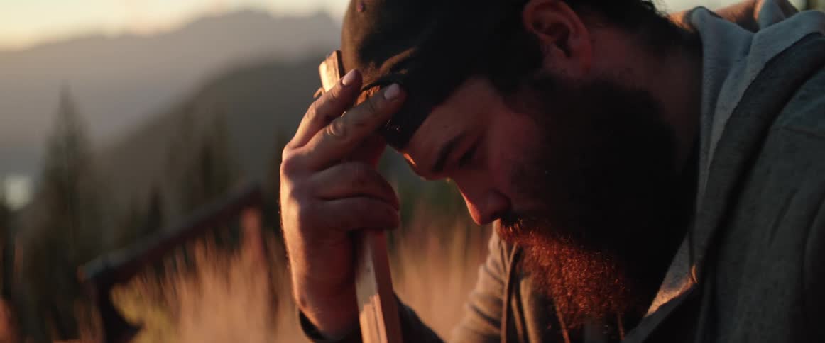 A man out in the wilderness adjusts his hat at sunset