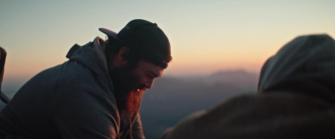 The sun sets as two men are outside laughing while distant mountains can be seen