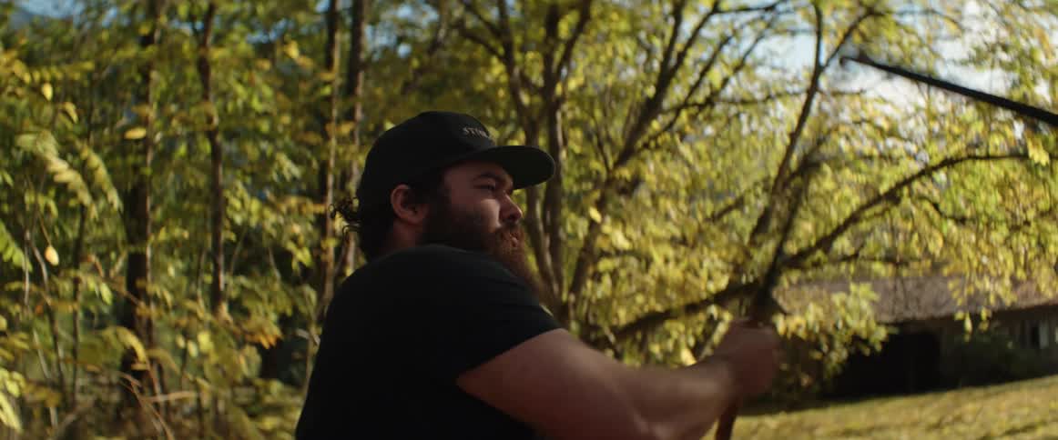 A man is outdoors in a field and doing Arnis combat with someone else