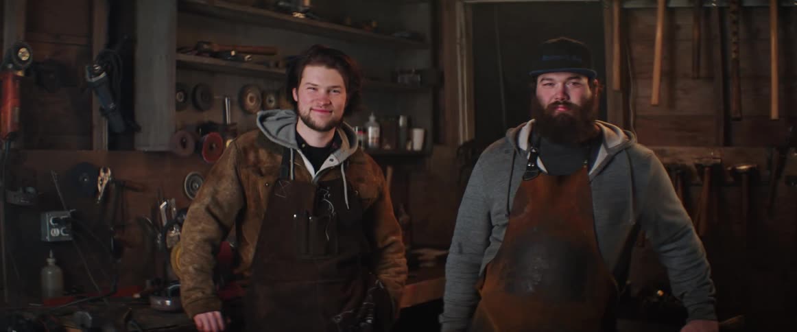 Two apron wearing craftsmen stand smiling in workshop