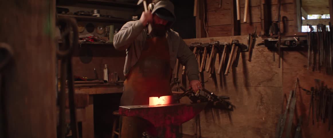 Blacksmith takes a piece of red hot iron from the forge and starts hammering it over the anvil