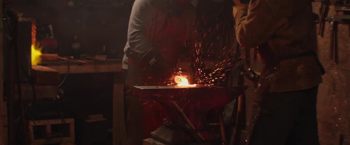 An explosion of sparks erupts from blacksmiths hitting hot metal on an anvil