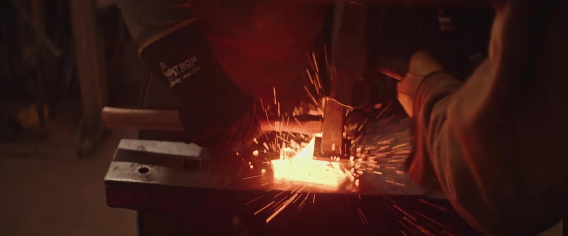 A blacksmith pounding a hammer on sparking molten metal over an anvil