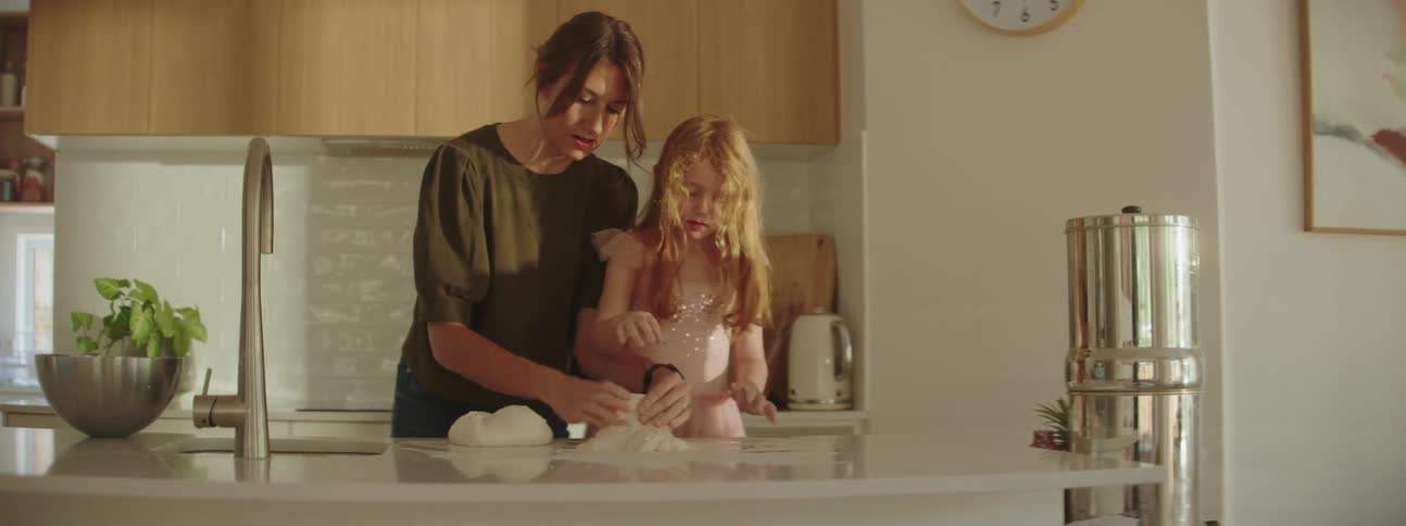 Women helping little girl knead dough on the counter