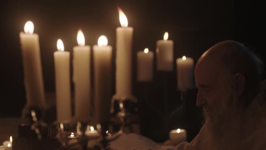 A man is sitting at a table with candles all over