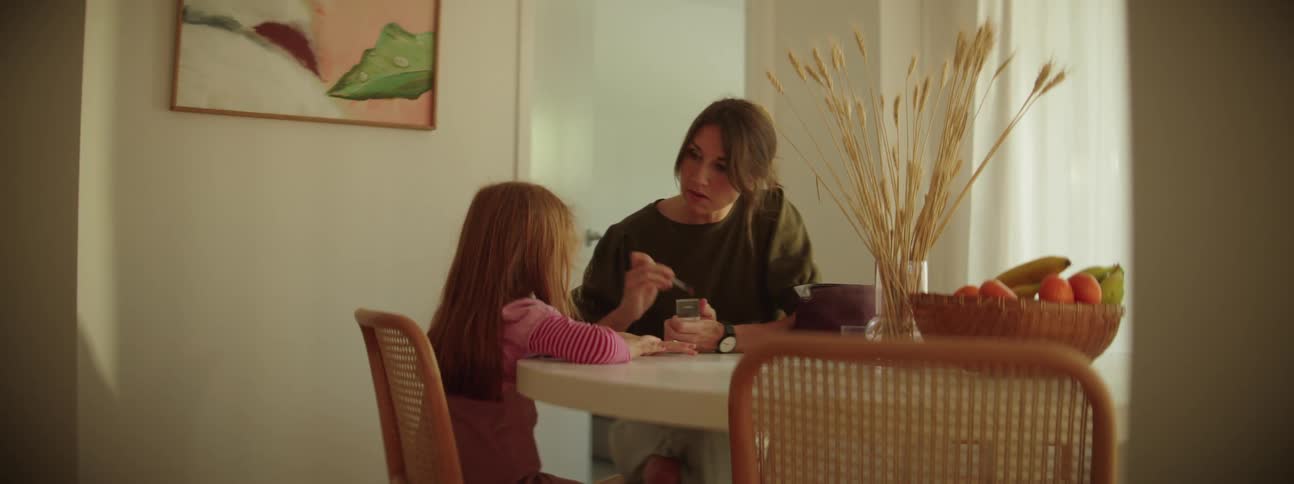 Mother with brown hair and black shirt does makeup on daughter sitting at table