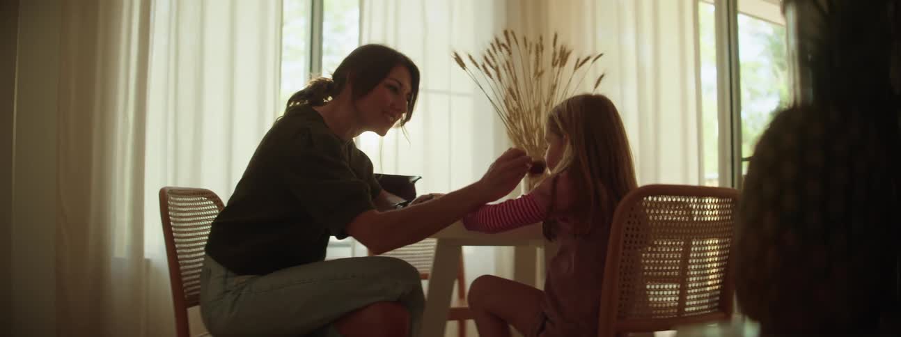 Mother teaches daughter how to apply makeup while sitting at the table at home