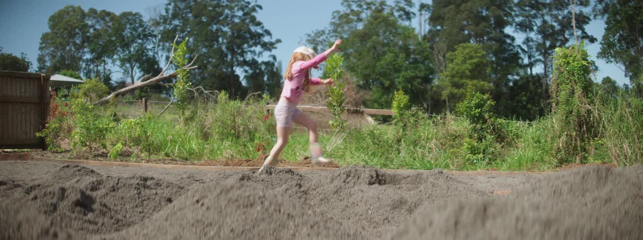 Girl wearing pink clothes playfully walks and jumps over loose sand in the countryside