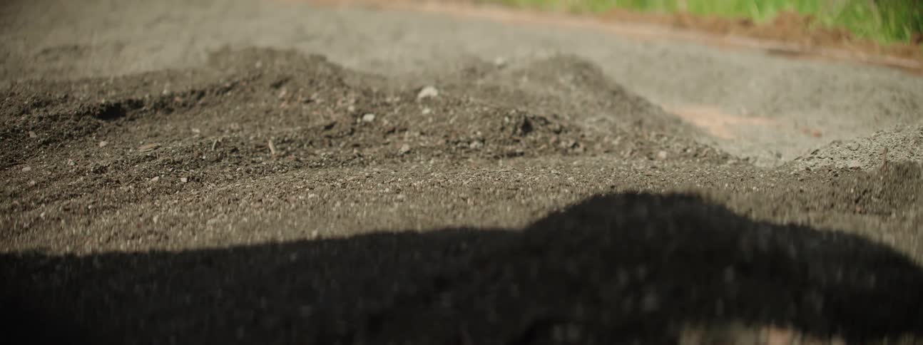 A person rakes gravel on a pathway in the backyard at daytime