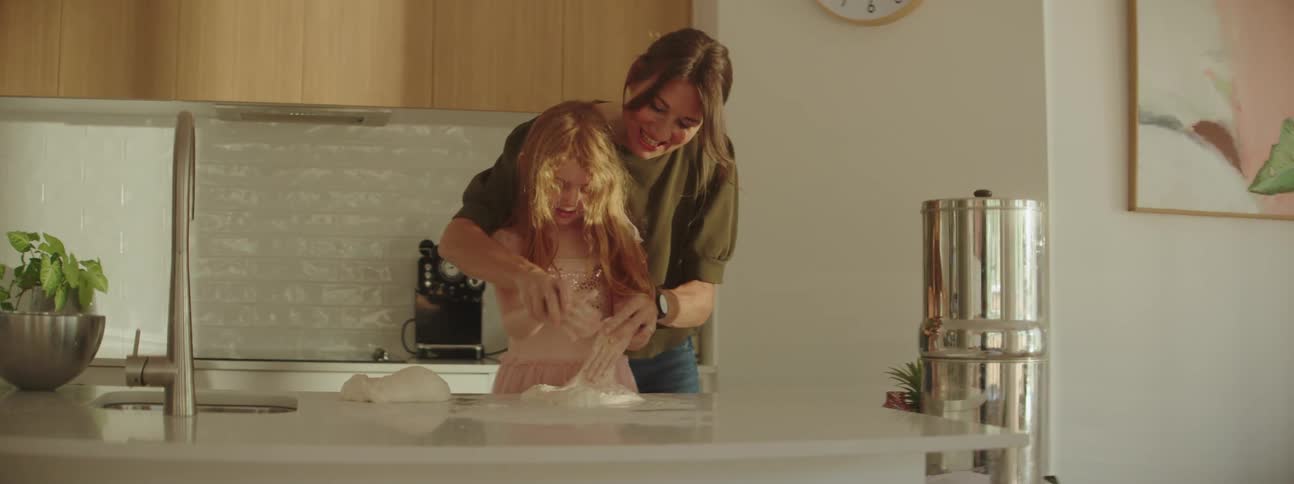 Women helping little girl knead dough on the kitchen counter