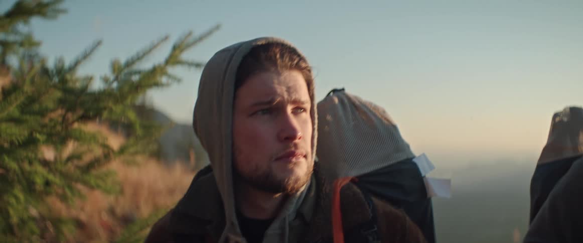 Men wearing hoodies and jackets carry bags along mountain trail at sunset
