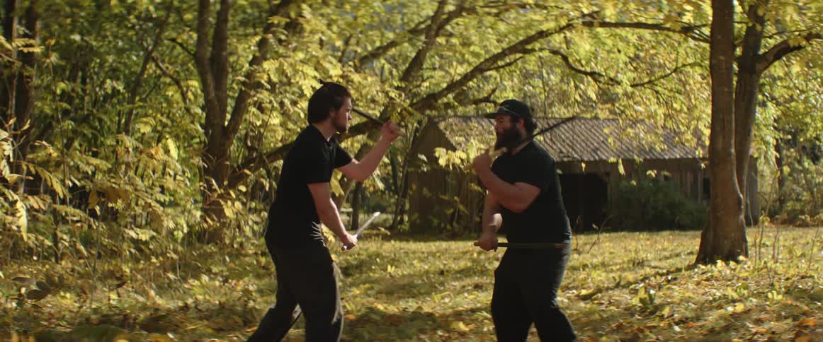 Two men fight each other using sticks in a rural field