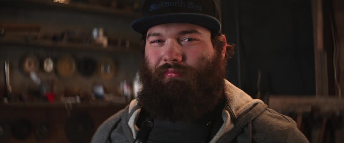 A portrait of a man with a beard standing inside a workshop