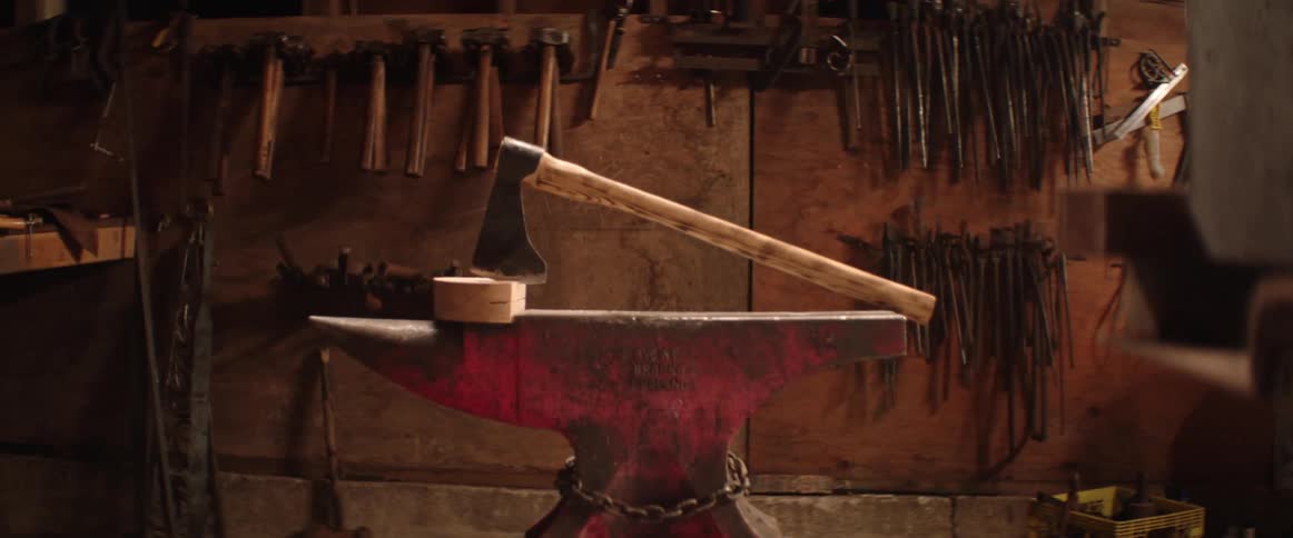 An ax is stuck in a piece of wood sitting on an anvil in a workshop