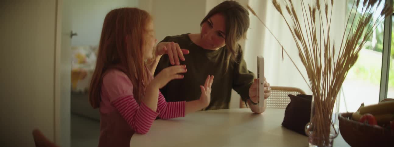 Mother holds a mirror in front of her daughters face inside a room at home