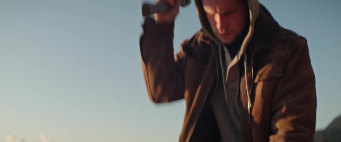 Man chops wood with a hatchet with distant mountains in the background