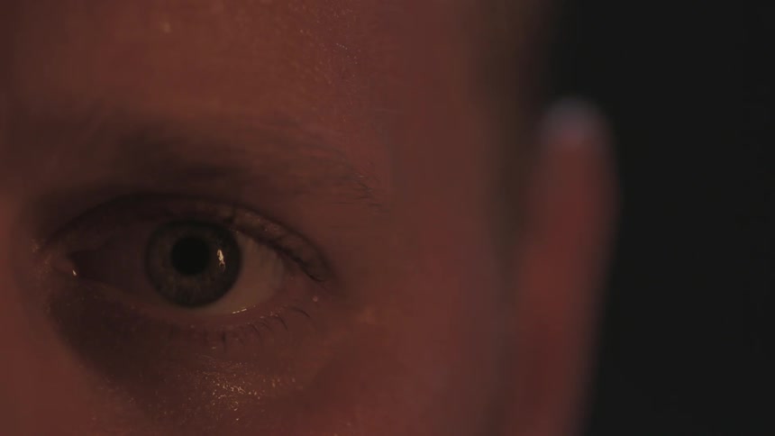 A man slowly opens his eye as light flickers on him