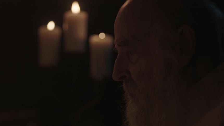 A man is sitting by some candles in a dark room