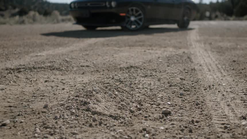 A muscle car sits in the sun on a dirt surface