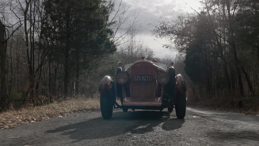 An antique car being driving down a road