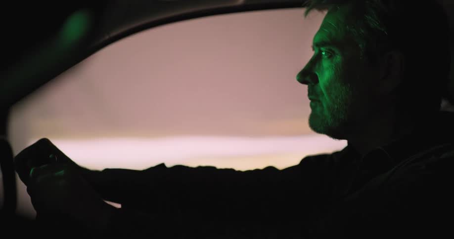 Side profile of man driving car in illuminated city street