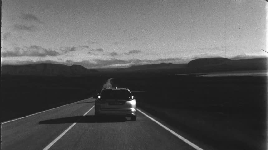An automobile travels on an open road with mountains in the distance