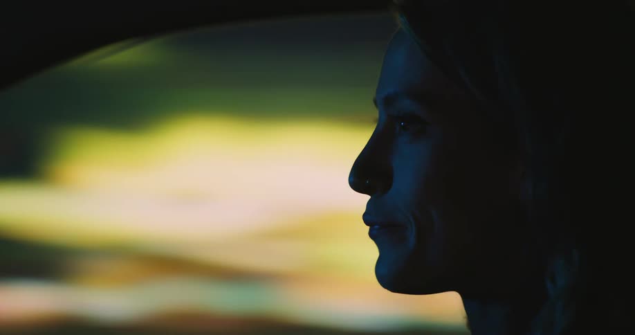 Close, profile of a woman sitting in a car with colorful with blurred city lights seen out of the window