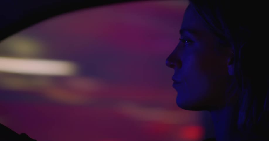 A woman drives a car with a blurred cityscape seen though the window